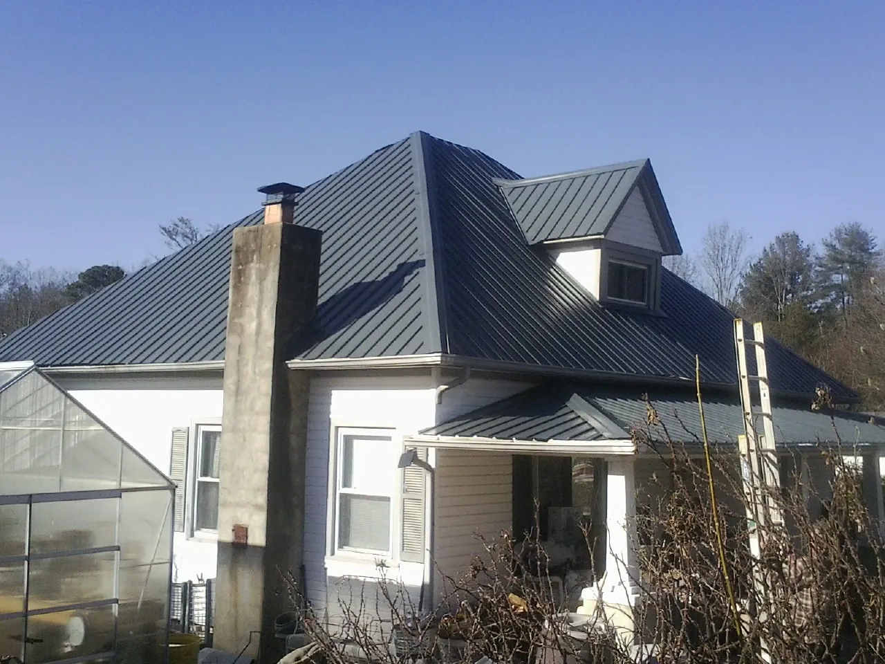 Dark blue standing seam metal roof on a white farmhouse with dormer — Slate & Tile Roof Repair by Roofing Brothers in Mocksville
