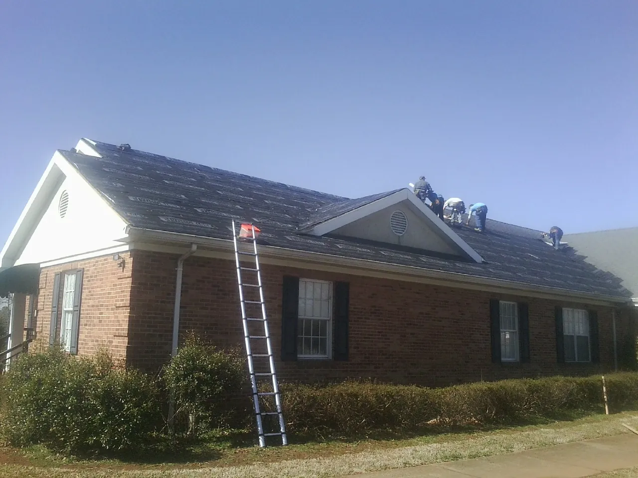 Crew tearing shingles off a brick ranch roof with a ladder set — Metal Roof Repair work by our crew in Mocksville