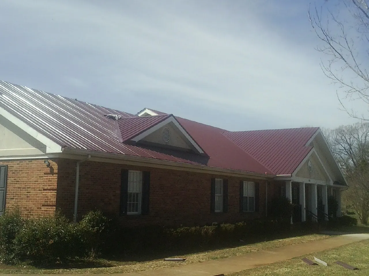Red metal roof with gabled entries on a long brick building, from a Hail Damage Roof Repair job in Mocksville