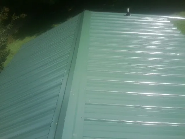 New green metal panels meeting at the ridge of a roof — Flat Roof Repair work by our crew in Mocksville