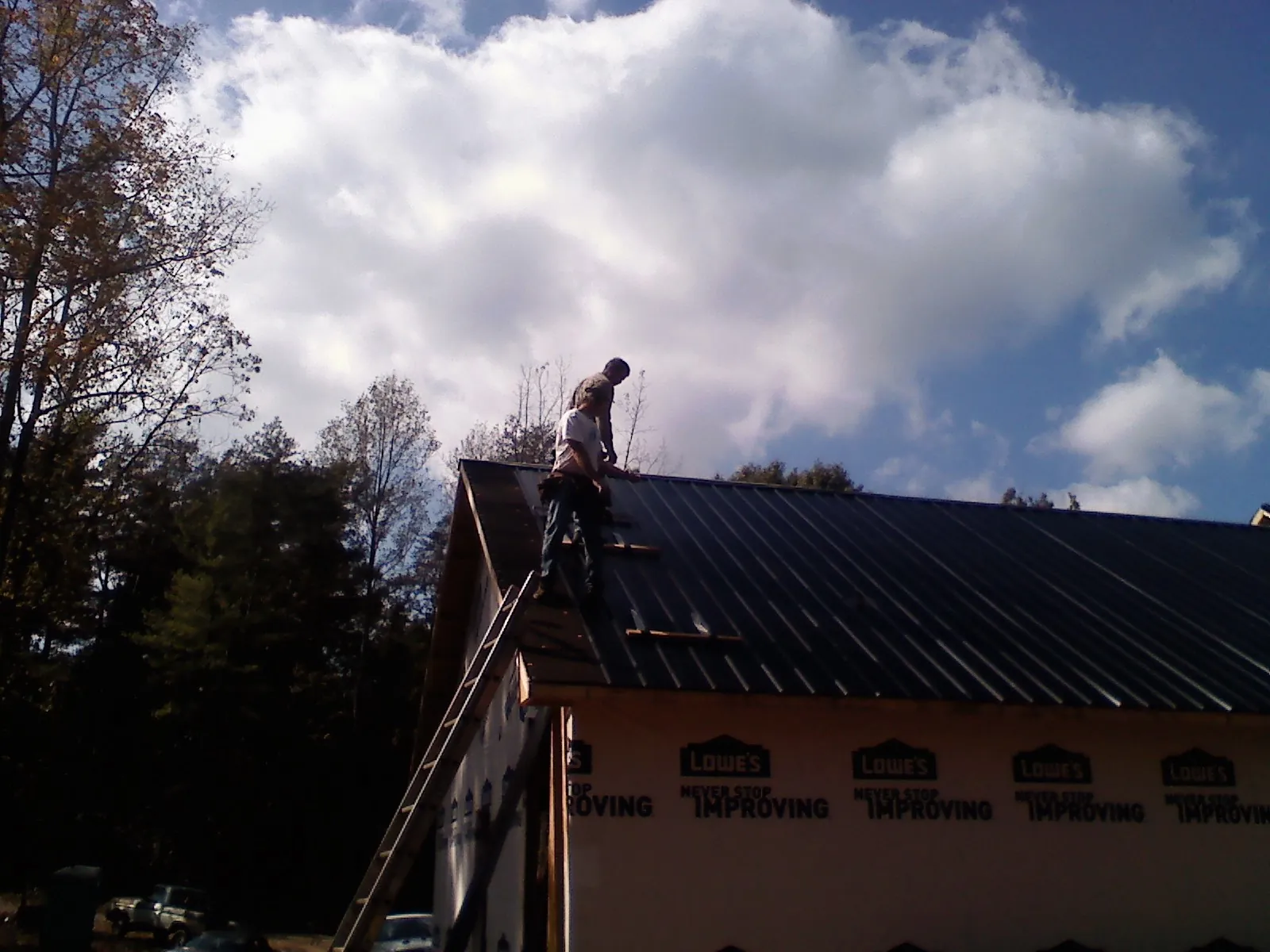 Roofer fastening dark metal panels high against a cloudy sky, from a Roof Inspection job in Mocksville