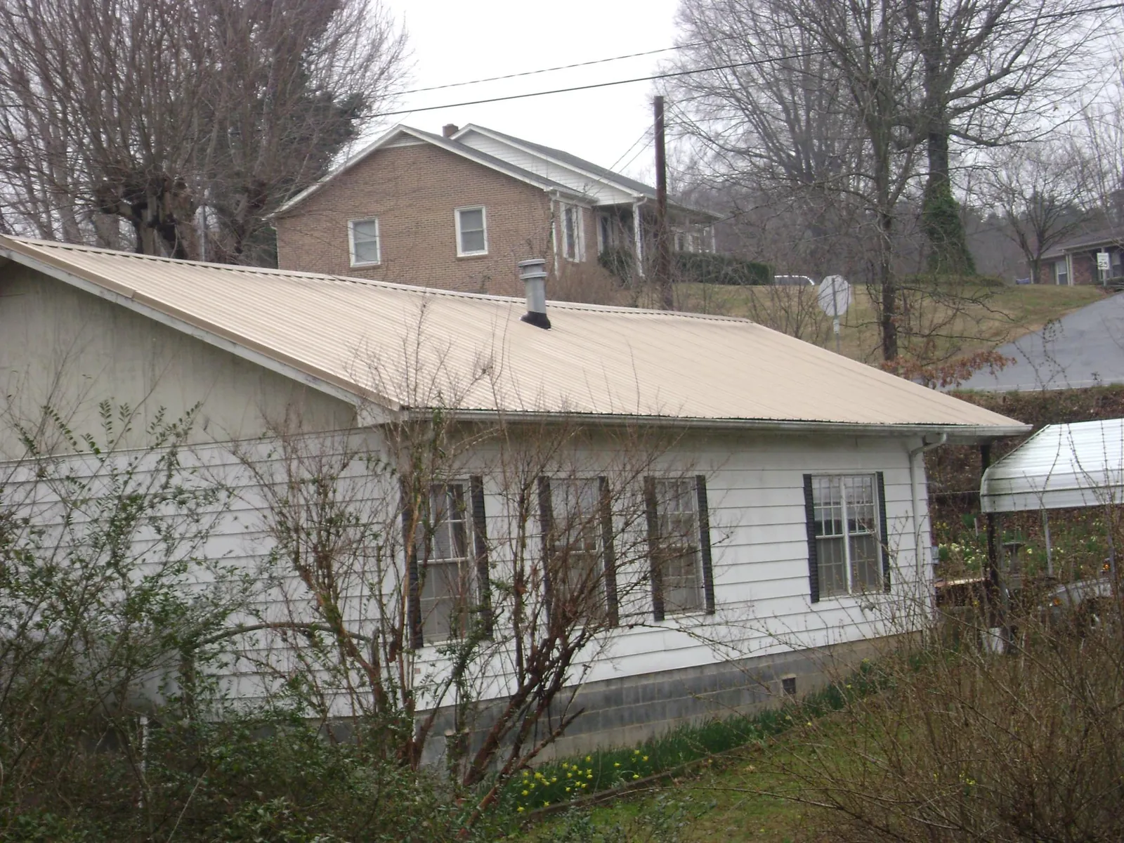 Tan metal roof on a white sided house set into a hillside — Commercial Roofing by Roofing Brothers in Mocksville